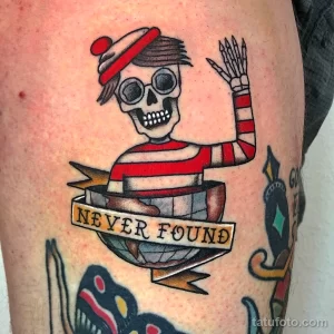 Фото тату скелета в шляпе и с надписью "Never Found" на руке. Рисунок татуировки выполнен в стиле олд скул с использованием ярких цветов.
