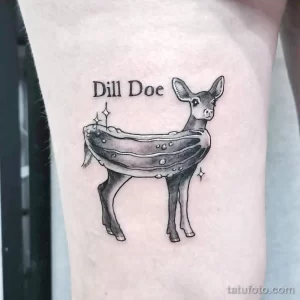 Фото тату олененка с надписью "Dill Doe" и блестками на руке. Рисунок татуировки выполнен в минималистичном стиле с использованием черного цвета.