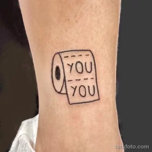Минималистичное фото тату рулона туалетной бумаги с надписью 'YOU YOU' на белой коже предплечья.