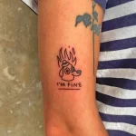 Фото тату: мультяшная собака с огнем вокруг головы и надписью 'I'M FINE' на предплечье.