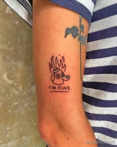 Фото тату: мультяшная собака с огнем вокруг головы и надписью 'I'M FINE' на предплечье.