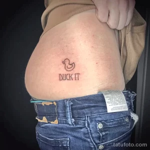 Фото тату: небольшое изображение утки с надписью 'BUCK IT' на животе.