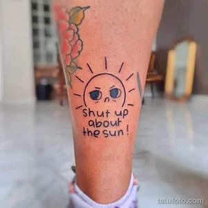 Фото тату: мультяшное солнце с грустным лицом и надписью 'shut up about the sun!' на предплечье.