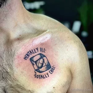 Фото тату: реалистичный рисунок кубика льда с надписью 'Mentally Ill: Totally Chill', выполненный в черных чернилах на груди. Эскиз татуировки выглядит провокационно и иронично.
