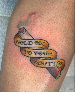 Цветное тату в стиле олдскул на руке с изображением сигары и надписи 'HOLD ON TO YOUR BUTTS'. Классический рисунок татуировки.