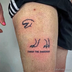 Фото тату, изображающего голову динозавра и три ноги, с надписью "FINISH THE DINOSAUR".