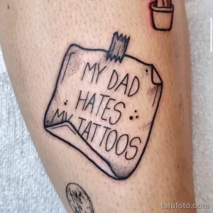 Фото тату, изображающего клочок бумаги с надписью "MY DAD HATES MY TATTOOS", прикрепленный к коже.