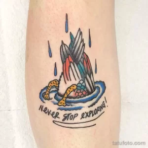 Фото татуировки горы, окруженной водой и дождем, с надписью 'Never Stop Exploring!'. Рисунок выполнен в традиционном стиле с яркими цветами.