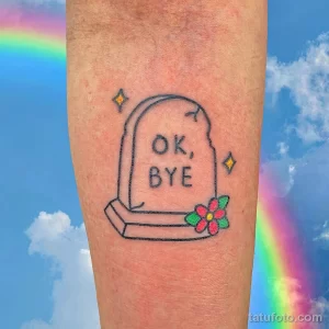 Фото тату надгробия с надписью "OK, BYE" и цветами. Рисунок выполнен в ярком и минималистичном стиле.