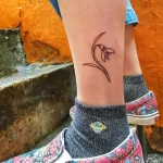 Фото тату подснежника на лодыжке. Черный контур, тонкие линии, простой и элегантный дизайн. Идеи для небольших тату на ноге.