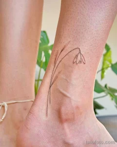 Минималистичное фото тату подснежника на женской лодыжке. Тонкие линии, черно-белый рисунок, нежный и элегантный дизайн.