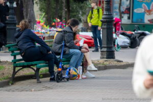 Фотография татуировки с изображением красной розы на ноге девушки, сидящей на скамейке в парке. Видны детали рисунка и окружающая обстановка.