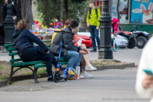 Фото татуировки с изображением красной розы на ноге девушки, сидящей на скамейке в парке. Видны детали рисунка и окружающая обстановка.