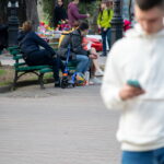 Фото татуировки с красной розой на ноге девушки, сидящей на скамейке в парке. Видны детали рисунка и окружение.