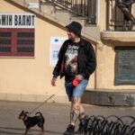 Фото тату на ногах мужчины, гуляющего с собакой на улице. Видны детализированные рисунки татуировок на голенях и бедрах.