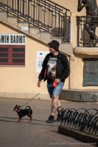 Фото тату на ногах мужчины, гуляющего с собакой на улице. Видны детализированные рисунки татуировок на голенях и бедрах.