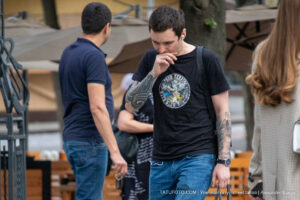 Фотография мужчины с татуировкой на руке, идущего по улице в черной футболке и джинсах.