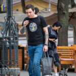 Фотография мужчины с татуировкой на руке, идущего по улице в черной футболке и джинсах.