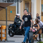 Фото тату на руке мужчины: детализированный рисунок в черных тонах, рука и плечо украшены татуировкой, городской фон, мотоцикл на заднем плане.