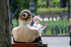 Фотография девушки сзади, демонстрирующая татуировку на шее. Татуировка выполнена в минималистичном стиле и изображает ветку с листьями.