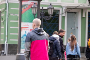 Фотография мужчины с короткой стрижкой и татуировкой в виде креста на шее. Он одет в яркую розово-серую куртку и смотрит в сторону.