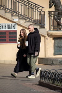 Фото уличной татуировки: мужчина и женщина с татуировками на руках, держащие стаканы кофе.