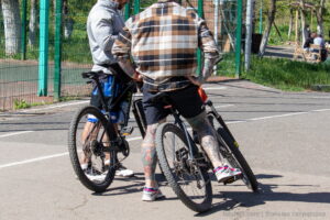 Фото тату на ногах мужчины, едущего на велосипеде. Детализированные цветные рисунки в японском стиле, покрывающие голени и бедра.