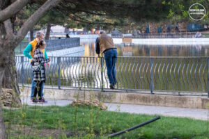 Фотография группы людей, стоящих у перил и смотрящих на воду. Видна река или озеро и отражение неба в воде.