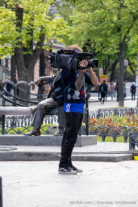 Фото тату на руке оператора, снимающего видео. Видна часть татуировки в ярких цветах, выполненной в стиле традишнл.