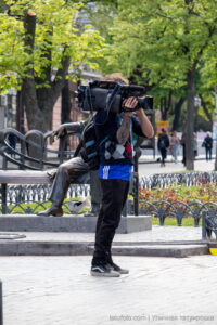 Фото тату на руке оператора, снимающего видео. Видна часть татуировки в ярких цветах, выполненной в стиле традишнл.