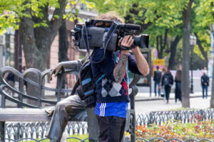 Фото тату на руке оператора, снимающего видео. Видна часть татуировки в ярких цветах, выполненной в стиле традишнл.