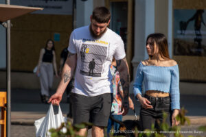 Фото мужчины с татуировками на руках и в футболке с ярким принтом. Татуировки выполнены в черном цвете, а принт на футболке сочетает желтый, черный и белый цвета.