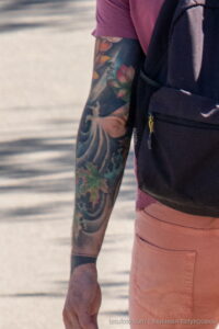 Фотография татуировки на руке мужчины в японском стиле. Изображены цветы, волны и другие традиционные элементы, выполненные в ярких цветах.