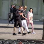 Фото мужчины с татуировкой на ноге, идущего по улице в черной одежде. Детализированный рисунок татуировки с изображением абстрактного узора.