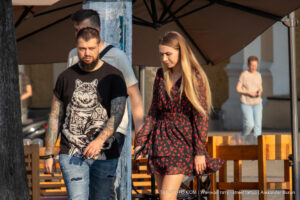 Фото тату на руке мужчины с изображением волка в скафандре космонавта. Рядом с ним идет девушка в красном платье.