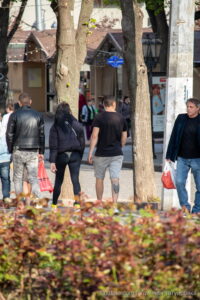 Фото тату волка на голени мужчины, выполненное в геометрическом стиле с использованием черных линий и точек. Виден общий план улицы.