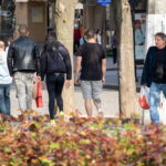 Фото тату волка на голени мужчины, выполненное в геометрическом стиле. Виден общий план улицы и людей.