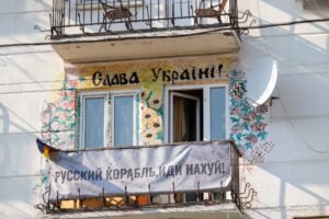 Фотография фасада дома, украшенного яркими рисунками и надписями в поддержку Украины. На балконе висят флаги и плакаты.