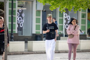 Фото татуировки на руке мужчины, идущего по улице. Видны детали рисунка татуировки, выполненной в темных тонах. Уличная фотография.