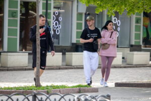 Фото татуировки на руке мужчины, идущего по улице. Видны детали рисунка татуировки, выполненной в темных тонах. Уличная фотография.