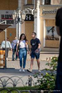 Фотография пары, идущей по улице, у мужчины видна татуировка на руке, выполненная в черном цвете. Городской пейзаж, солнечный день.