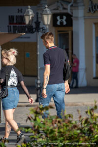 Фото тату на предплечье мужчины, выполненное в темных тонах. Мужчина идет по улице в повседневной одежде.
