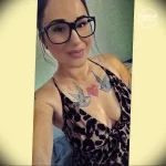 Фотография девушки в очках с татуировкой двух голубей на груди, вид спереди.
