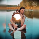 Фотография девушки, сидящей в воде с антикварным зеркалом в руках, с татуировкой на плече.