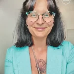 Фото татуировки на груди девушки, изображающей цветок с тонкими линиями и листьями. Тату выполнено в минималистичном стиле в черно-серых тонах.