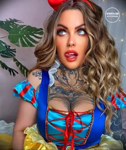 Фотография девушки в костюме Белоснежки с яркими и детализированными татуировками на груди и шее. Тату изображают цветы, животных и абстрактные узоры.
