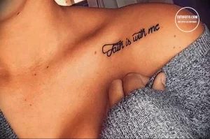 Фото тату: небольшая надпись 'Faith is with me' на ключице, выполненная элегантным шрифтом.