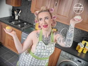Фотография девушки в фартуке и бигуди с татуировками на руках. Видны детализированные рисунки в стиле графика.