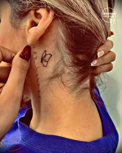 Фото тату: небольшая татуировка в виде бабочки и надписи 'end tattoo' на шее девушки, выполненная в тонких линиях и красном цвете.