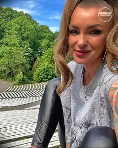 Фотография девушки с татуировками на руках, позирующей на фоне зеленого парка.